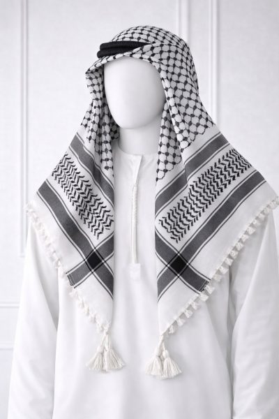 Classic white keffiyeh shemagh scarf featuring black geometric patterns and tassel edges worn over a white thobe for a traditional Arabic look.