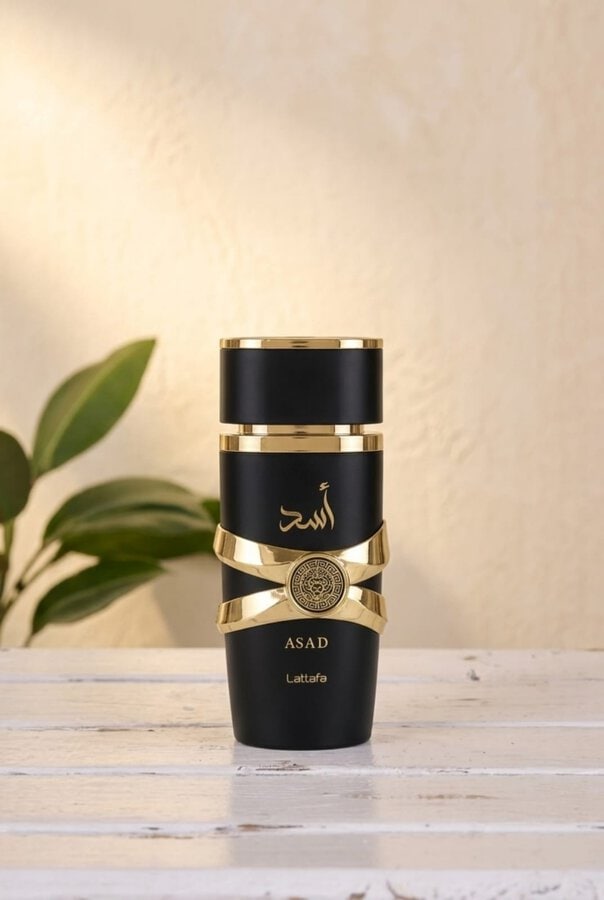 Lattafa Asad 100ml perfume for men in a luxury black and gold bottle with a circular lion crest shield next to its original packaging box.